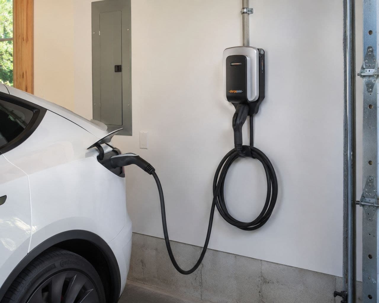 White electric vehicle plugged into a wall-mounted ChargePoint charging station in a garage.