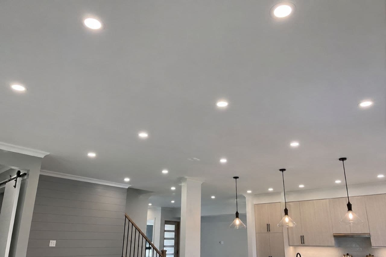 Modern white ceiling with numerous recessed lights and three glass pendant lights over a kitchen.