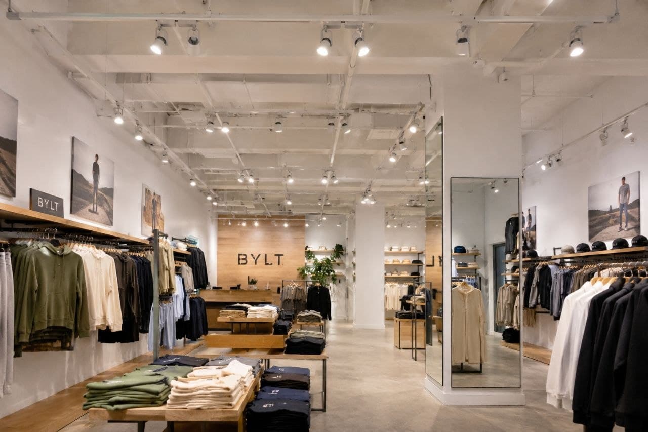 Minimalist BYLT retail store interior featuring organized clothing racks, folded apparel, and bright track lighting.